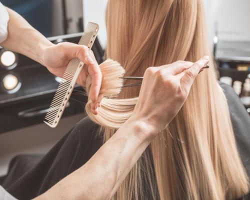 Kampaaja leikkaa vaaleahiuksisen naisen hiusten latvoja